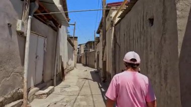 Pembe tişörtlü ve şapkalı bir kadın Buhara 'nın eski dar sokaklarında yürüyor. Özbekistan, Orta Asya 'ya seyahat. Tarih, turizm ve macera