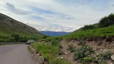 Kazakistan 'a araba yolculuğu. Yeşil tepeleri ve dağları geçmek için yol boyunca arabayla gidiyorum. Kazakistan 'ın kırsal kesimlerinde trafik vardı. Seyahat ve Macera