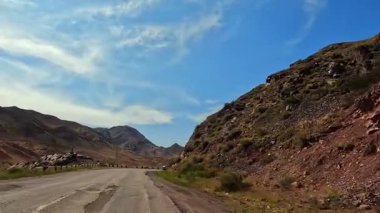 Kazakistan 'ın yolları. Orta Asya 'da arabayla seyahat ediyor. Uçurumlar, tepeler, dağ yamaçları ve yol boyunca uzanan beyaz bulutlu mavi bir gökyüzü. Turizm ve özgürlük