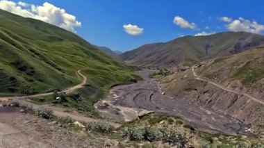 Güzel yeşil bir dağ vadisinde kurumuş bir nehir yatağının havadan görünüşü. Azerbaycan 'a araba yolculuğu. Köye giden toprak yolu olan bir dağ sırası..