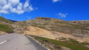 Azerbaycan 'da bir yerlerde yüksek bir dağ yolunda at sürüyor. Dağ yolunun muhteşem manzarası, yeşil kayalık tepeler, mavi gökyüzü ve kumlu yamaçlar..