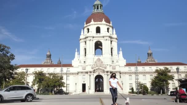 Kobieta w masce na twarz spacerujący pies w ratuszu Pasadena w pustych ulicach miasta — Wideo stockowe