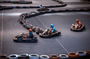 Üç adam kapalı bir karting pistinde birbirini solluyor.