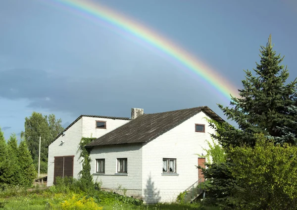 The bright rainbow over the village house in late afternoon light (Lithuania).