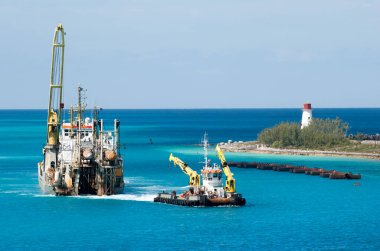 Endüstriyel gemi ve vinçleri olan bir römorkör Paradise Island deniz fenerinin yanından geçer (Bahamalar).