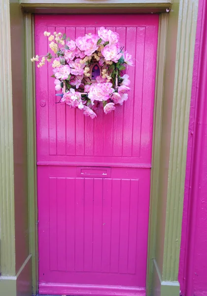 pink door with floral wreath and fairy door