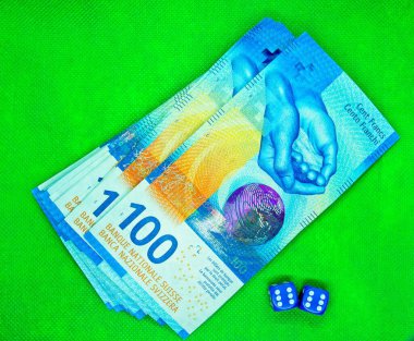 Yeşil arka planda, iki mavi zarın yanında çekilmiş.