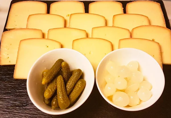 Raclette cheese tray with small onion bowls and pickles