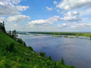 Nehir kıyısına yakın güzel yeşil bir yamaç. Gökyüzüne karşı. Güzel bir manzarada harika bulutlar.