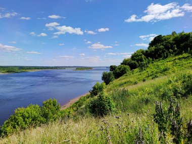 Nehrin yanındaki yeşil dağ yamacında güneşli bir günde bulutlu mavi gökyüzüne karşı.