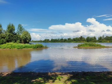 Nehirdeki yeşil adacıklar, güneşli bir günde bulutlu mavi gökyüzünün arka planına karşı.