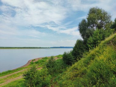 Nehir kıyısının yanındaki yeşil yamaçta bulutlu mavi bir gökyüzüne karşı