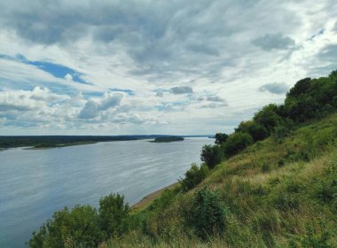 Kıyı şeridine yakın yeşil dağ yamacında mavi bulutlu gökyüzüne karşı
