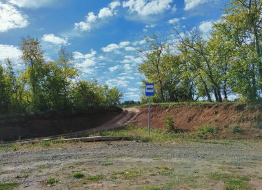 Ağaçların ve mavi gökyüzünün arka planında güneşli bir günde bulutlu minimalist otobüs durağı