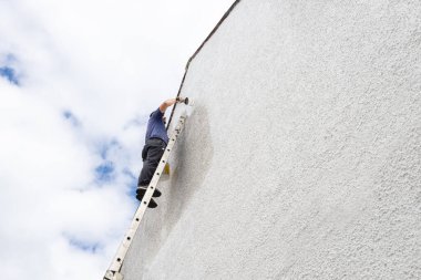 Çalışkan bir adam, yüksek bir merdiven, evin kenarını beyaz bir renge boyar..