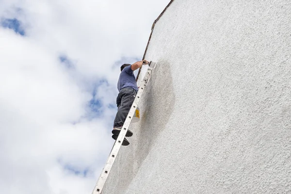 Man uppför en hög stege målning gaveln änden av sten hus. — Stockfoto