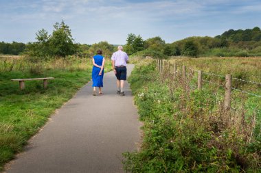 Yaşlı çift, güneşli bir günde İngiliz kırsalında yol boyunca yürür..