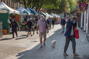 Yüzü maskeli bir adam güneşli bir günde köpeğiyle Canterbury High Caddesi 'nde yürüyor..