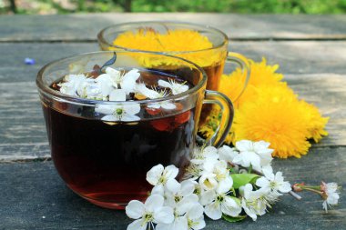 İki bardak şeffaf çay, beyaz ve sarı güzel bahar çiçekleri ormandaki ahşap bir masada..