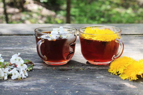 İki bardak şeffaf çay, beyaz ve sarı güzel bahar çiçekleri ormandaki ahşap bir masada..