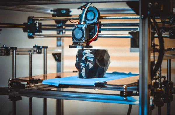 3D printer printing a model in the form of black skull close-up.