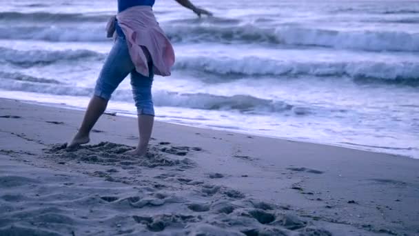 Девушка в синих джинсах и розовой куртке, завязанной на поясе, вышла в море — стоковое видео