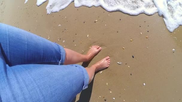 La fille est debout près de la mer et les vagues la roulent sur ses pieds — Video