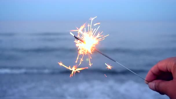 Branden van een Bengalen brand in de hand tegen de achtergrond van een zee — Stockvideo