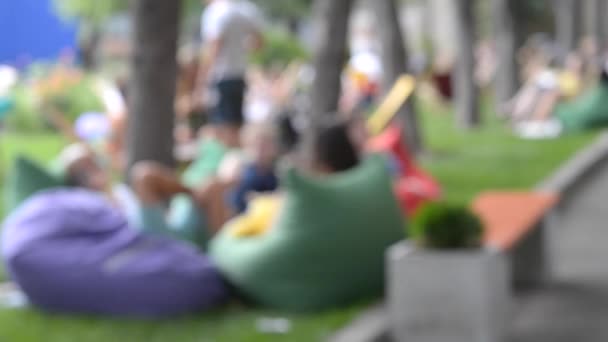 Rozmazané pozadí lidé odpočinku v tašce židle, křesla tašky v parku — Stock video
