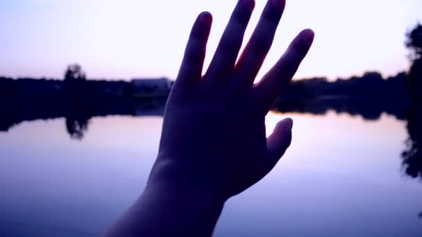 Черный силуэт руки перемещает его в воздухе, сквозь пальцы сквозь лучи солнца — стоковое видео
