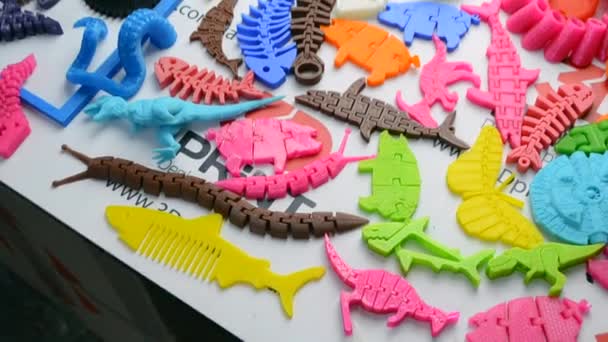 Muitos objetos multicoloridos brilhantes impressos em uma impressora 3D estão em uma superfície plana — Vídeo de Stock