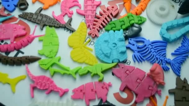 De nombreux objets multicolores lumineux imprimés sur une imprimante 3D reposent sur une surface plane — Video