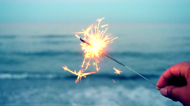 Quemando un fuego de Bengala en la mano contra el fondo de las olas del mar — Vídeos de Stock