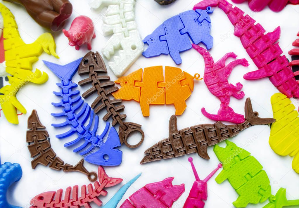 Many bright multi-colored objects printed on 3d printer lie on flat surface