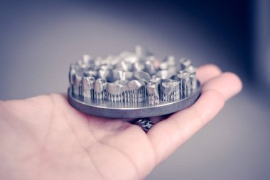 Metal 3D yazıcıya yazdırılmış nesneyi tutan adam.