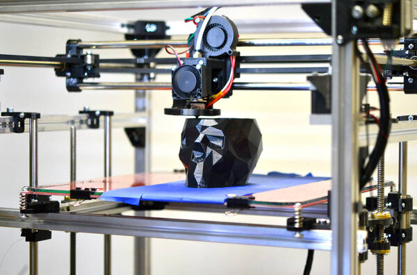 3D принтер печатает модель в виде черного черепа крупным планом
