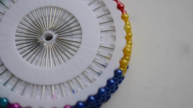 Bir terzi kadın, beyaz disklerdeki plastik başlıklı iğneyi çıkarır. Terziye çok renkli bir iğne al ve yerine geri koy.