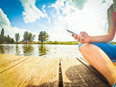 Bir kız onun elinde bir telefon ile ahşap yüzeyinde oturur