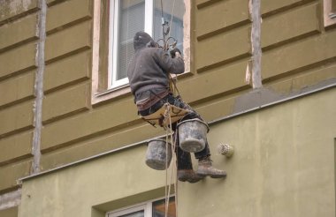 The man works on high-rise works cladding, plastering of the house clipart