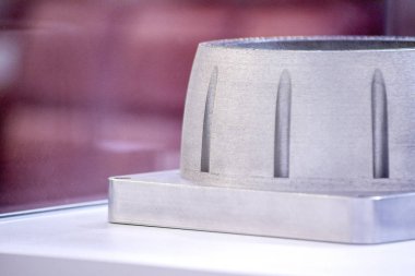 Metal 3D yazıcıya yazdırılmış nesneyi tutan adam.