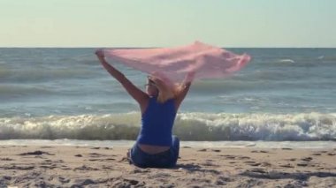 Pembe eşarplı kız sahilin kumlu sahilinde oturuyor.