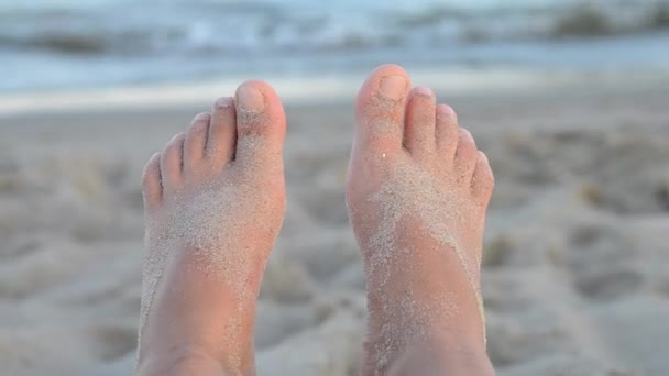 Zwei Füße mit Sand übersät vor den Wellen des Meeres im Licht des Sonnenaufgangs — Stockvideo