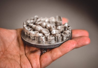 Metal 3D yazıcıya yazdırılmış nesneyi tutan adam.