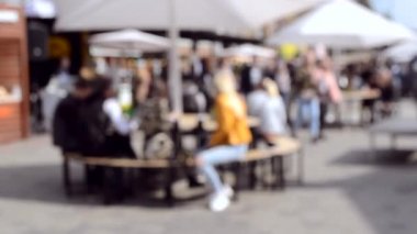 İnsanlar şemsiyeli masalarda oturup yemek yerler.