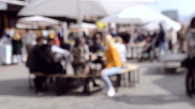 İnsanlar şemsiyeli masalarda oturup yemek yerler.