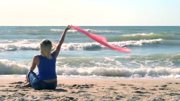 Menina com um lenço rosa está sentado na costa arenosa da praia — Vídeo de Stock