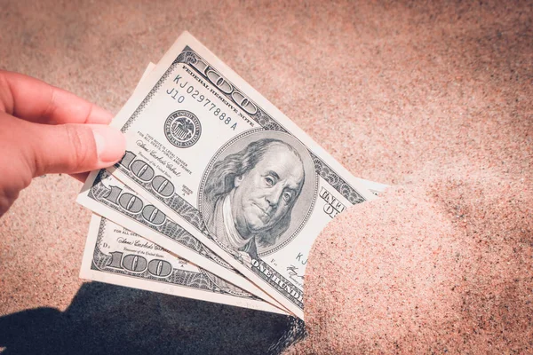 A girl takes out from the sand money notes of three hundred dollars.
