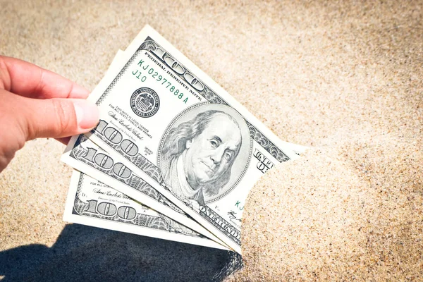 A girl takes out from the sand money notes of three hundred dollars.