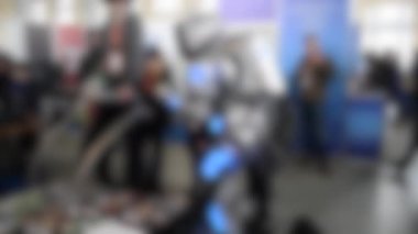 Arka plan bulanık. Robot kostümlü adam ziyaretçilerle iletişim kuruyor.