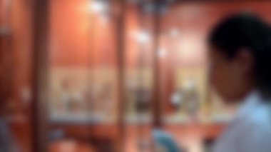 Arka plan bulanık. Genç bir kız telefonunun fotoğrafını çekmiş. Bunu vitrinde izliyor.